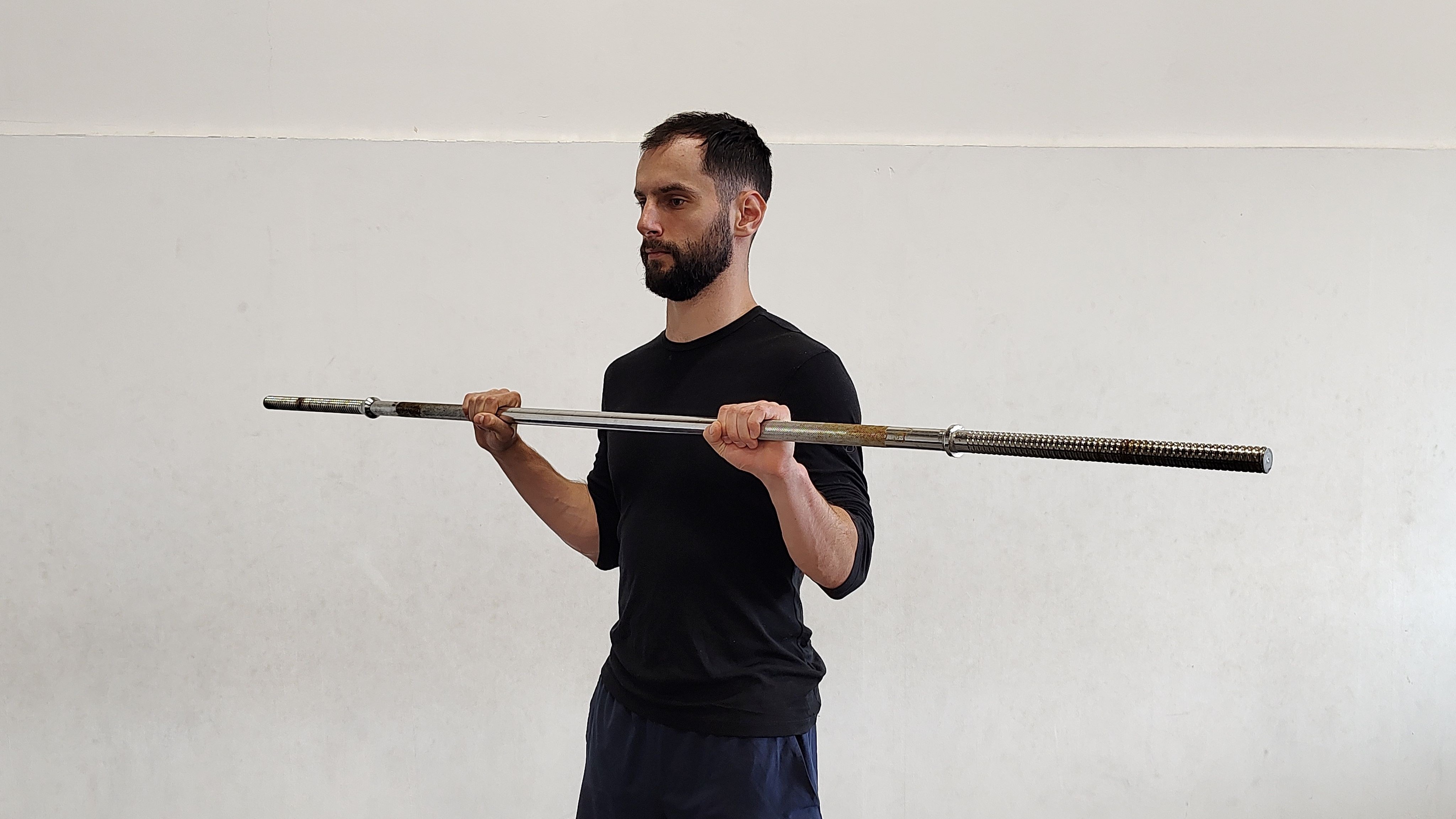Muž cvičí v tělocvičně bicepsový zdvih s osou s nadhmatem.